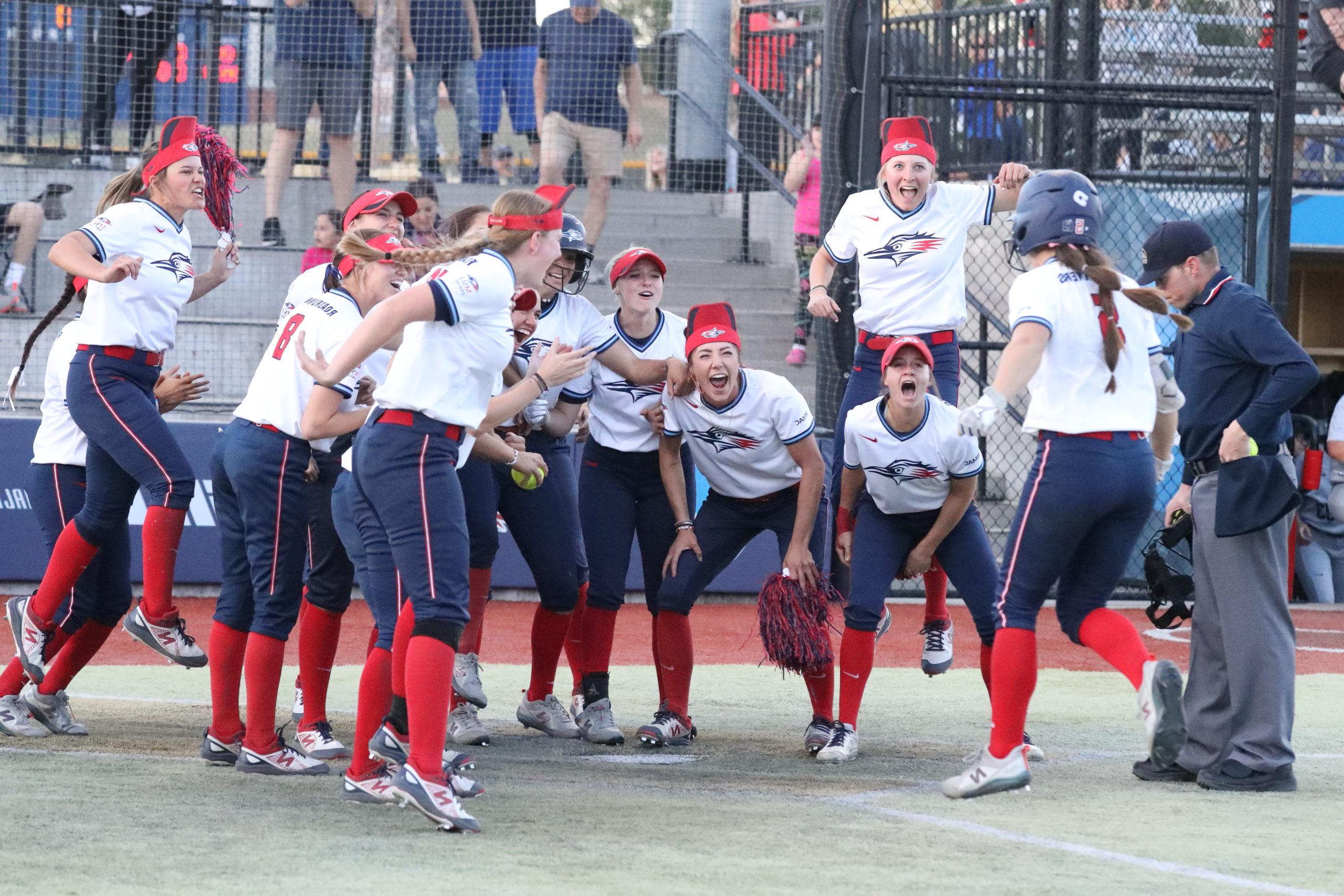 Softball player Shelby Robb approaches home plate after a walk-off home run as her teammates enthusiastically wait to greet her.