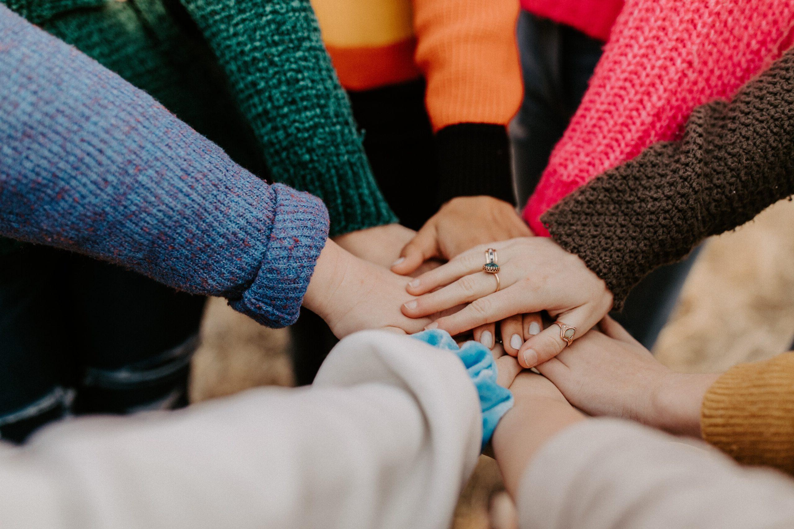 Several people with different colored long sleeves placing their hands on top of each other